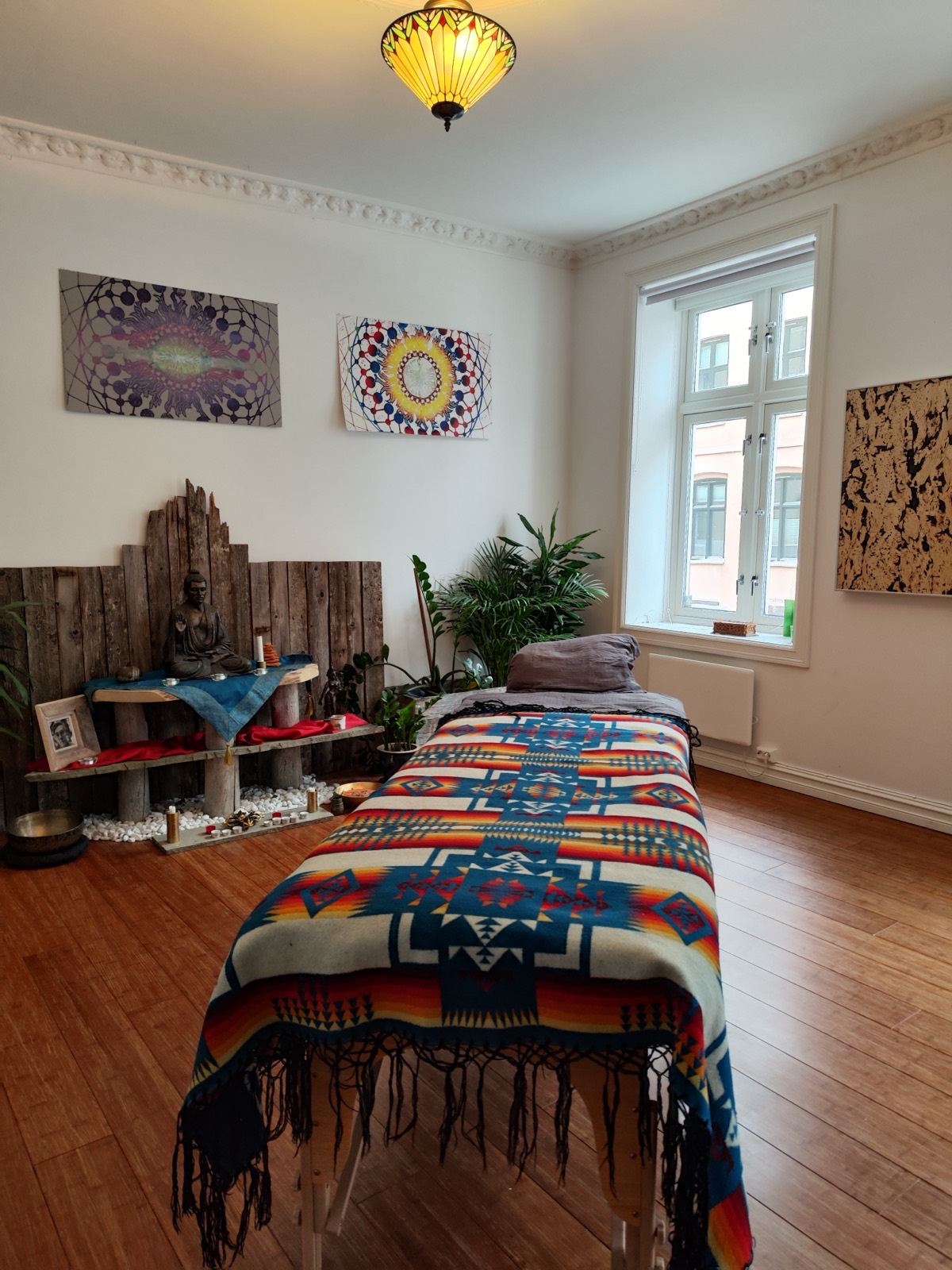 The treatment room in Grünerløkka, with a woven blanket on the treatment bench, plants and a small altar